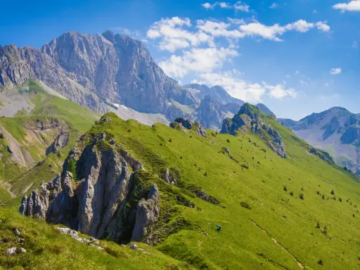 Prati verdi e sentieri invitano a **passeggiate facili** in Val Seriana, con maestose cime sullo sfondo sotto un cielo azzurro.