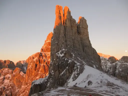 Le Torri del Vajolet illuminate dal caldo bagliore del tramonto, con la neve che ricopre le cime rocciose.