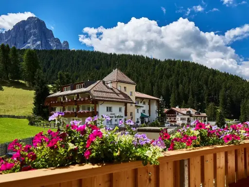 Fiori colorati su un balcone con vista su un hotel e le montagne, un'oasi di pace nei rifugi Val Gardena.