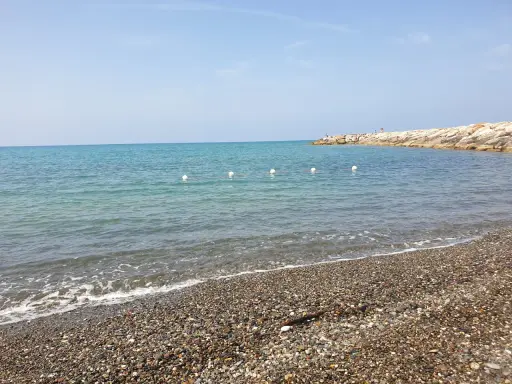 Spiagge più belle della Marina di Cecina: mare azzurro, ciottoli levigati e un molo roccioso con qualche bagnante.