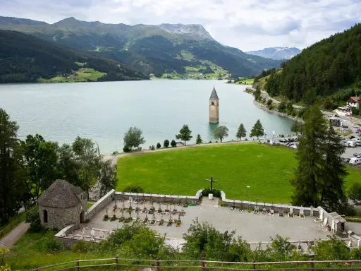 Un antico campanile nel lago, circondato da montagne verdi e un cimitero.