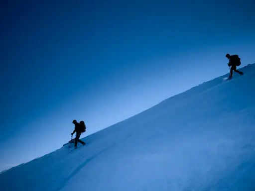 Due escursionisti con ciaspole salgono un pendio innevato sotto un cielo blu intenso. Le ciaspole sono perfette per camminare sulla neve fresca.