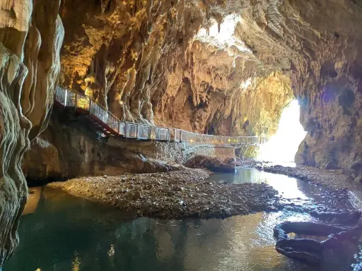 Sentiero illuminato lungo un ruscello nelle grotte di Pastena, tra stalattiti e stalagmiti dorate.