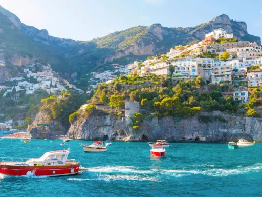 Barche a vela navigano nelle acque turchesi davanti alle case colorate aggrappate alle scogliere delle isole costiera amalfitana.