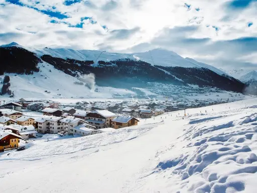 Paesaggio invernale con villaggio innevato e montagne sullo sfondo. Perfetto per sapere dove andare in montagna in Trentino per sciare.