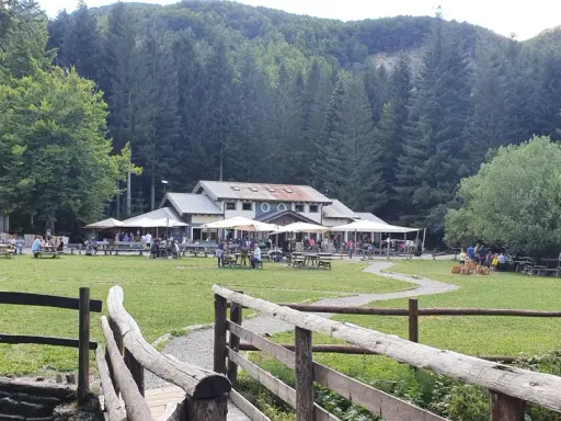 Un rifugio in Emilia Romagna immerso nel verde, con tavoli all'aperto e persone che si godono la giornata.