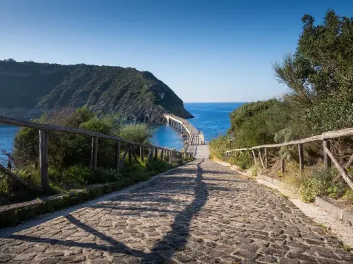 Sentiero acciottolato verso un ponte sul mare, ideale per cammini in Italia sul mare.