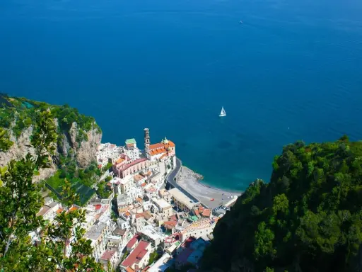 Vista dall'alto di Amalfi, con il mare blu intenso e una barca a vela. Il percorso da Amalfi a Ravello offre panorami mozzafiato.