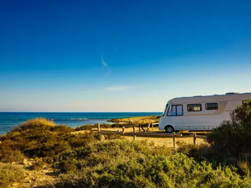 Un camper bianco sosta su un sentiero sabbioso con vista sul mare blu intenso. Un'avventura indimenticabile in camper all'Isola d'Elba.