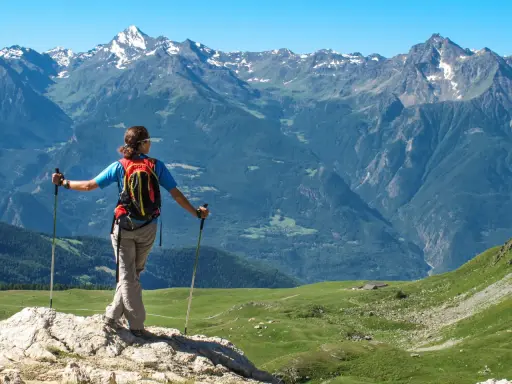 Escursionista con zaino e bastoncini ammira un panorama alpino mozzafiato, perfetto per scoprire gli itinerari della Valle d'Aosta.