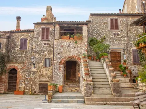 Antica piazza con case in pietra, scale in terracotta e piante rigogliose, un'atmosfera da **borghi medievali toscana**.