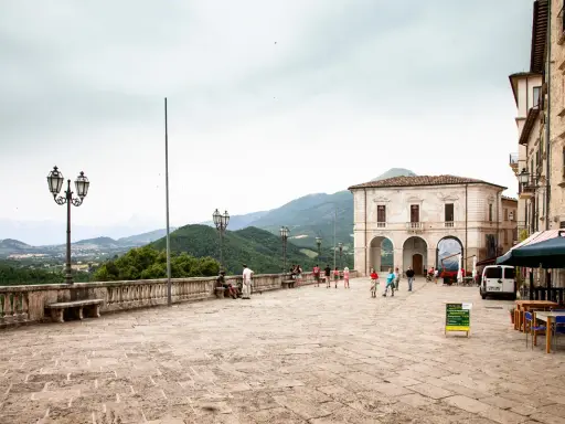 Piazza di Civitella del Tronto con edifici storici, gente che passeggia e vista panoramica sulle colline verdi.