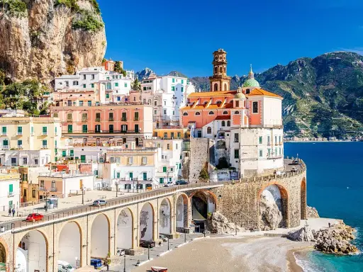 Un incantevole borgo da visitare in Campania, con case colorate aggrappate alla roccia, un ponte ad archi e il mare blu.