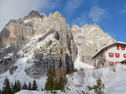 Rifugio alpino innevato ai piedi di maestose vette rocciose, un vero spettacolo di posti belli in montagna Veneto inverno.
