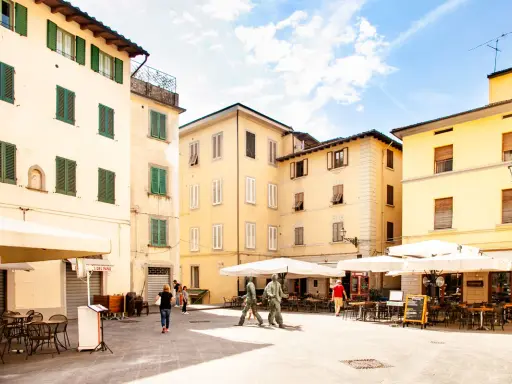 Piazza con edifici storici e tavolini all'aperto, ideale per scoprire cosa vedere a Pistoia in un giorno.