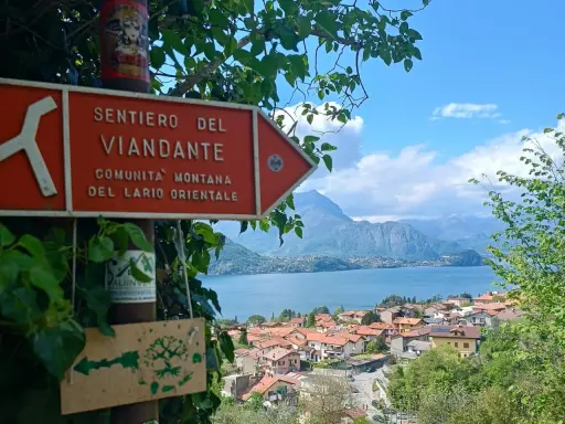 Segnale arancione indica "Sentiero del Viandante" con vista su un lago e montagne.