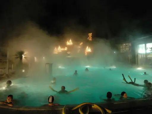 Persone si rilassano in una piscina termale notturna, con luci natalizie che brillano tra la nebbia, un'atmosfera magica nei bagni di Romagna.