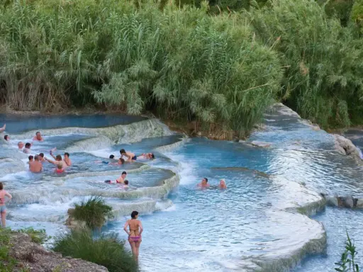 Persone si rilassano nelle cascate naturali delle terme famose in Italia, circondate da vegetazione lussureggiante.