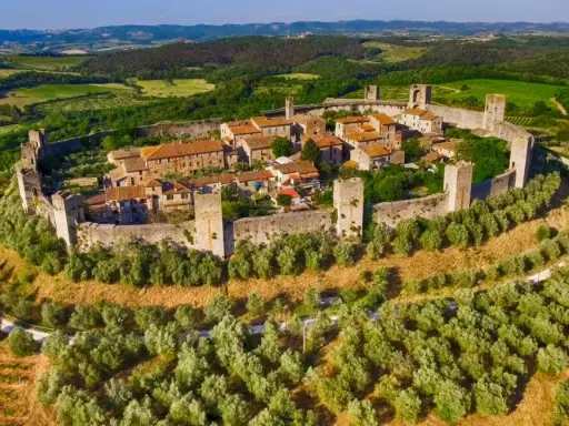 Borghi medievali fortificati vicino Siena, con mura imponenti e torri che dominano un paesaggio collinare verdeggiante.