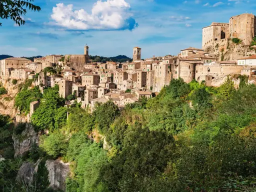 Un affascinante borgo toscano da visitare, arroccato su una rupe tufacea, con case in pietra e torri che si stagliano contro il cielo azzurro.