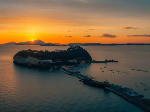 Tramonto infuocato sul golfo di Napoli, con una suggestiva isoletta che emerge dal mare calmo, illuminata dagli ultimi raggi dorati.
