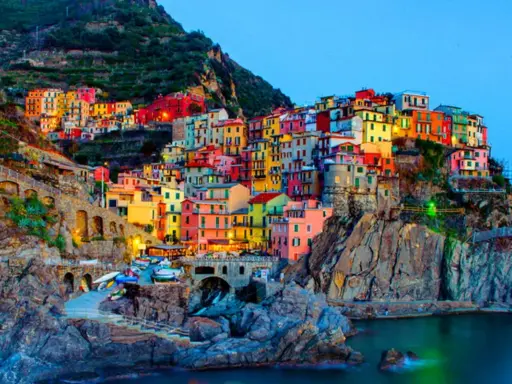 Case colorate aggrappate alla scogliera, un incantevole scorcio di quali sono le 5 Terre, con barche ormeggiate e il mare blu.