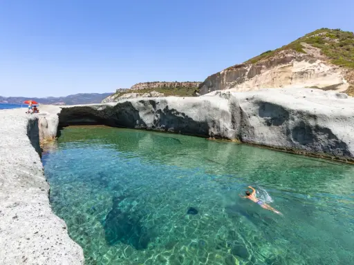 Un uomo nuota in acque cristalline tra scogliere bianche. Un luogo ideale per scoprire le spiagge di Bosa e cosa vedere.
