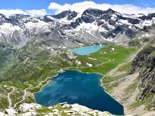 Laghi alpini blu e turchese ai piedi del Colle del Nivolet, con strade tortuose e montagne innevate sullo sfondo.