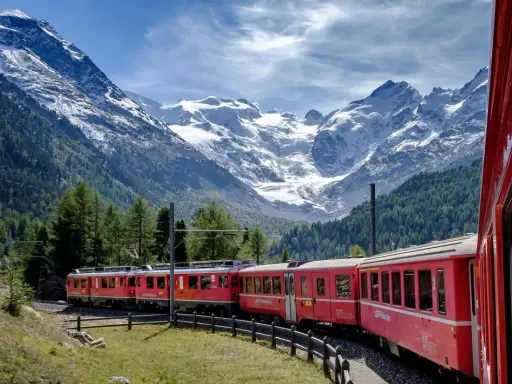 Treni panoramici rossi attraversano un paesaggio alpino mozzafiato con montagne innevate e foreste verdi.