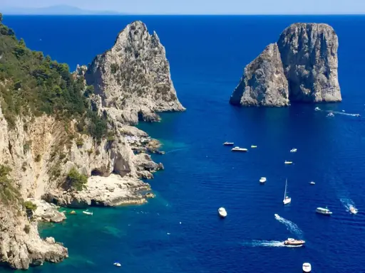 Faraglioni di Capri, tra le più belle isole di Napoli da visitare. Barche navigano nel mare blu intenso.