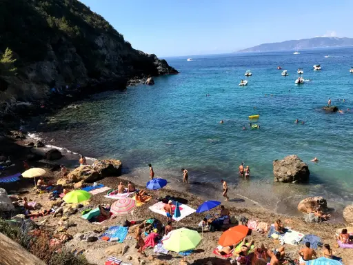 Spiaggia affollata con ombrelloni colorati e gente che nuota. Ecco come arrivare a Cala del Gesso per godersi questo mare cristallino.