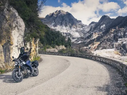 Motociclista su strada tortuosa con montagne di marmo sullo sfondo, un'autentica **Toscana da visitare**.