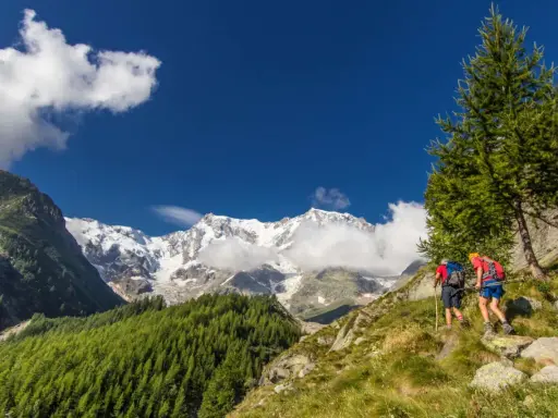 Due escursionisti affrontano un sentiero in Val d'Ossola, con maestose cime innevate sullo sfondo. Perfetto per escursioni facili.