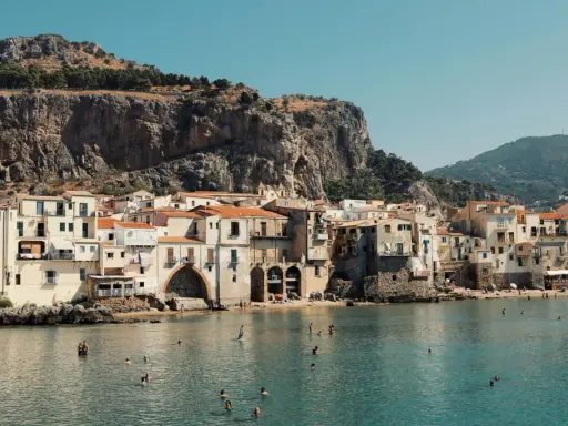 Un incantevole borgo da visitare in Sicilia, con case color pastello affacciate sul mare cristallino e una maestosa roccia a fare da sfondo.