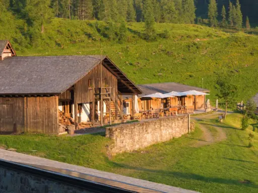 Malghe Alto Adige immerse nel verde, con rustici in legno e tavoli all'aperto sotto ombrelloni bianchi. Un'oasi di pace tra i boschi.