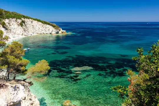 Scogliera bianca a picco sul mare cristallino della Toscana. Un angolo di paradiso con acque turchesi e vegetazione mediterranea.