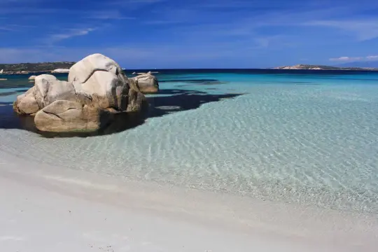Spiaggia bianca e rocce granitiche sull'isola della Maddalena, con acque cristalline e un cielo azzurro intenso.
