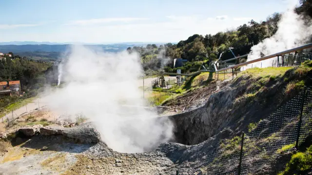 Il **parco delle Biancane** offre un percorso tra fumarole e sorgenti termali. Vapore acqueo sale da un cratere, con tubature industriali sullo sfondo.