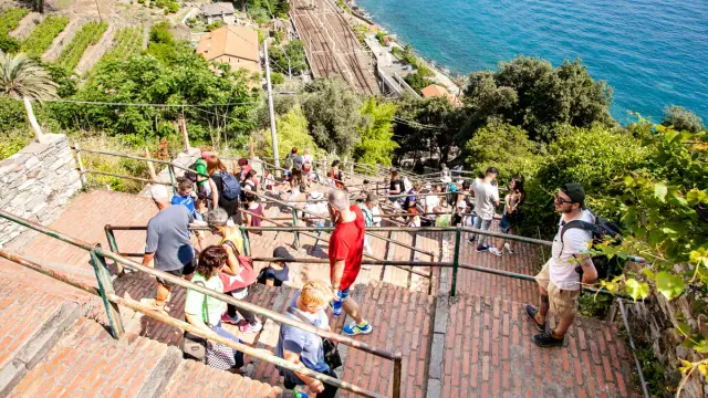 Turisti scendono la lunga scalinata di Corniglia, tra vigneti e il mare blu. Cosa vedere? La vista mozzafiato!