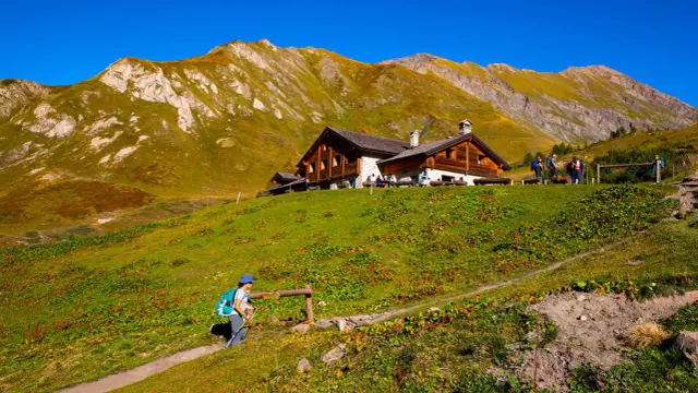 Un escursionista si avvicina a un rifugio in Valle d'Aosta, con montagne imponenti sullo sfondo.