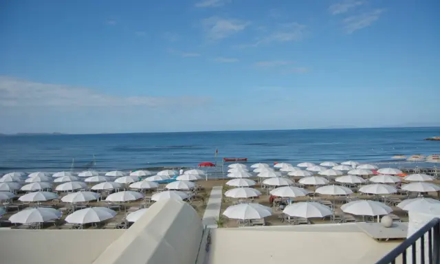 Spiaggia di **Marina di Follonica** con file ordinate di ombrelloni bianchi, mare azzurro e cielo sereno.