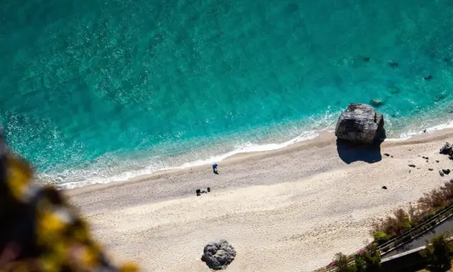 Spiaggia dorata e mare cristallino sulla riviera ligure di ponente. Un pescatore solitario e rocce imponenti.