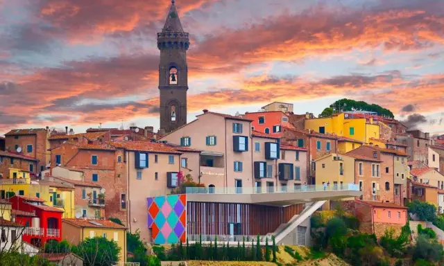 Un borgo italiano con case colorate e una torre campanaria, sotto un cielo infuocato. Potrebbe essere qual è il borgo più bello d'Italia.