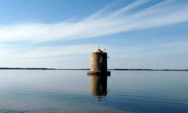 Mulino solitario nella laguna di Orbetello, con cielo azzurro e nuvole sottili.