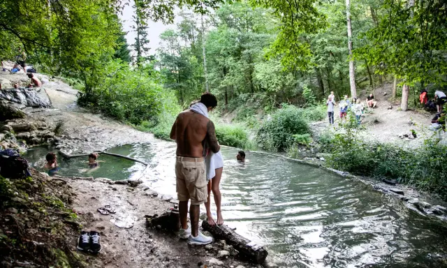 Persone si rilassano nelle acque termali dei Bagni di San Filippo, immersi nel verde di un bosco.