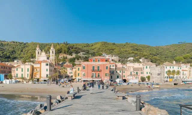 Laigueglia centro storico: case colorate affacciate sulla spiaggia, con una chiesa a due campanili e il mare azzurro.