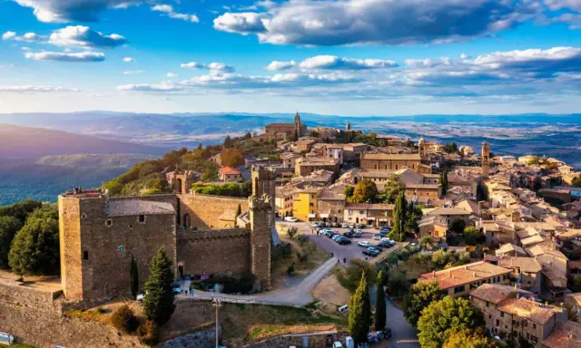 Un borgo medievale arroccato su una collina, tra i più belli d'Italia, con un castello imponente e case in pietra sotto un cielo azzurro.