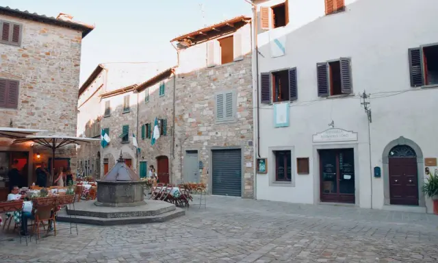 Piazza di San Donato in Poggio con pozzo antico, tavoli all'aperto e l'insegna "Osteria Numero Uno".