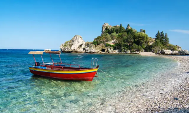 Barca rossa e gialla in acque cristalline, con isolotto verdeggiante sullo sfondo. Un angolo di paradiso che ricorda la bellezza di Sicilia e Sardegna.