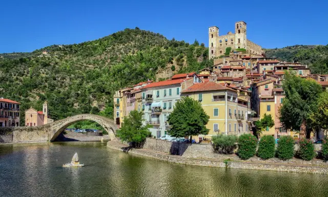 Borghi entroterra ligure levante: un ponte antico attraversa un fiume, case colorate si affacciano sull'acqua, un castello domina la collina verde.